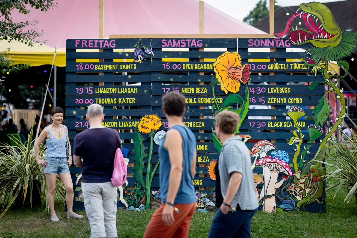 Timetable einmal anders: Beim H2U in Uster setzt man noch auf ein analoges Modell. Man sieht Menschen vor einer Tafel aus Holz, die mit Bands und Uhrzeiten angeschrieben ist.
